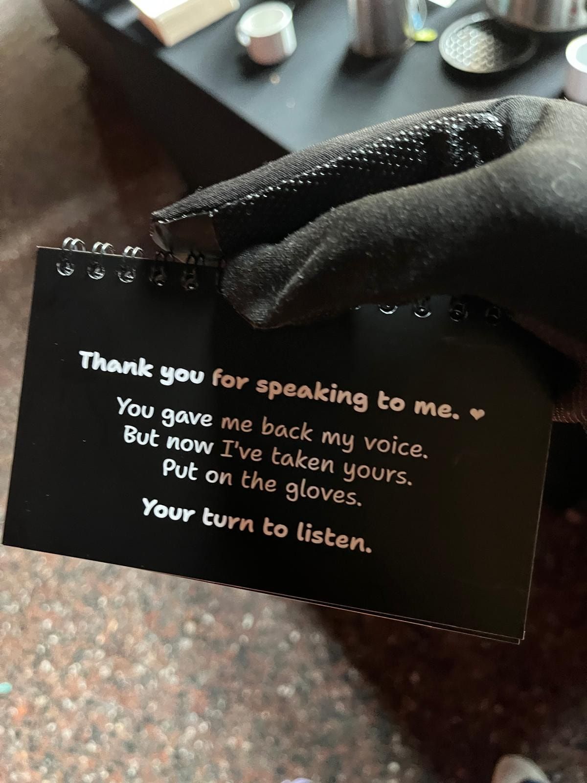 A card in the booklet reading: Thank you for speaking to me. You gave me back my voice. But now I've taken yours. Put on the gloves. Your turn to listen