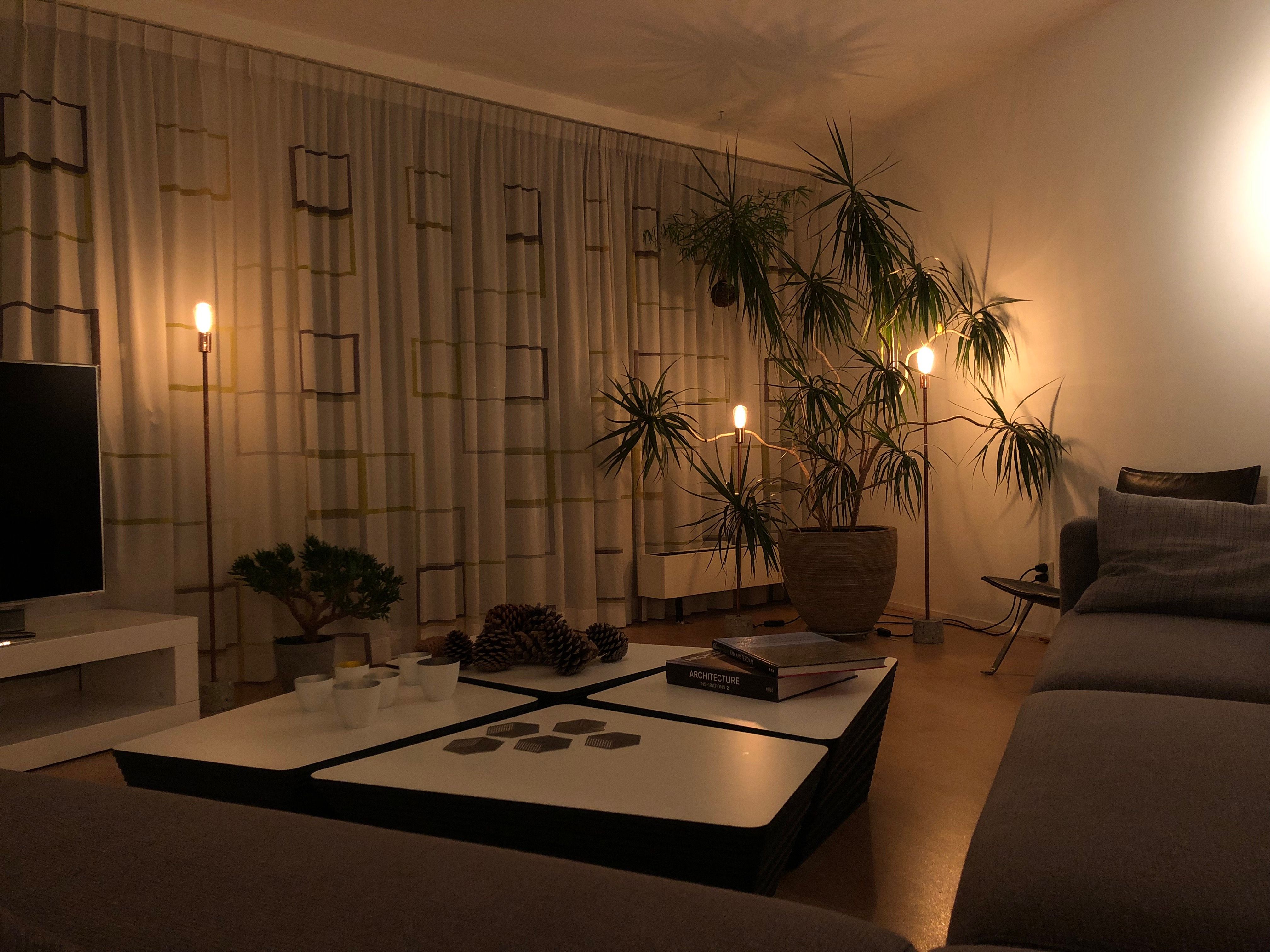 A dim living room lit by slim brass standing lamps with bare filament bulbs