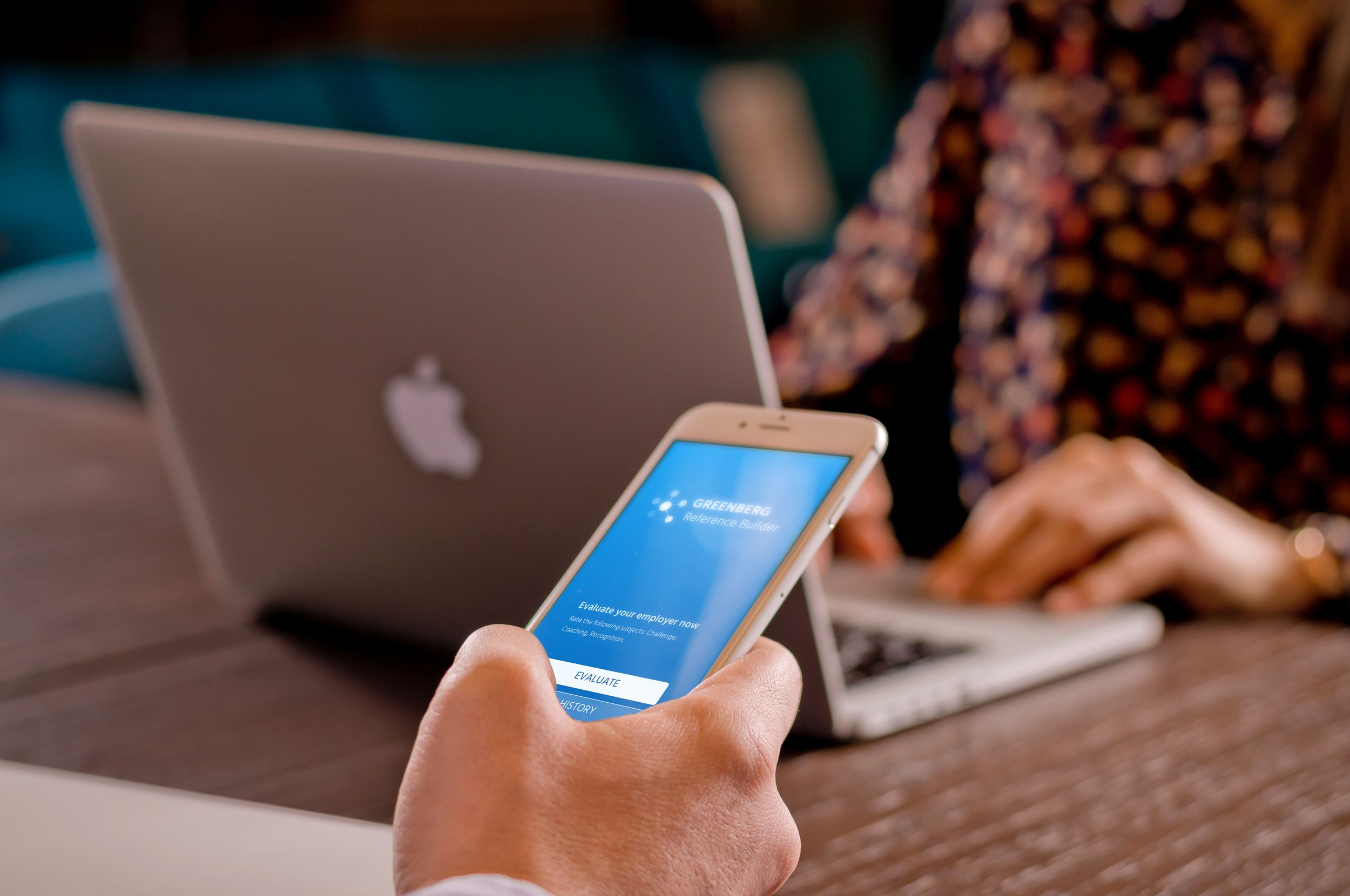 A hand holding a phone with the Reference Builder app, next to a laptop on a wooden table