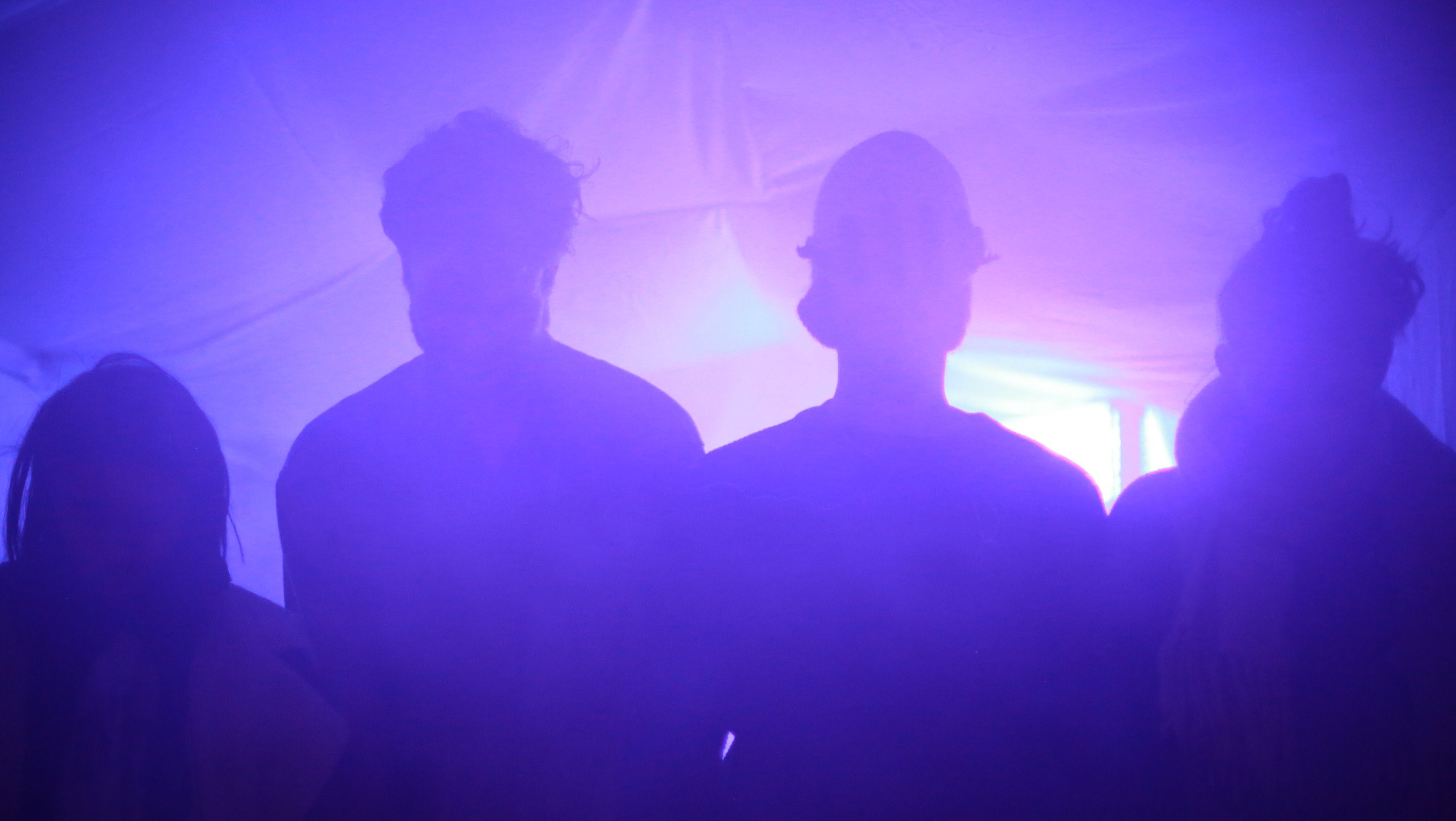 Silhouettes of four people against purple light and haze in a tent