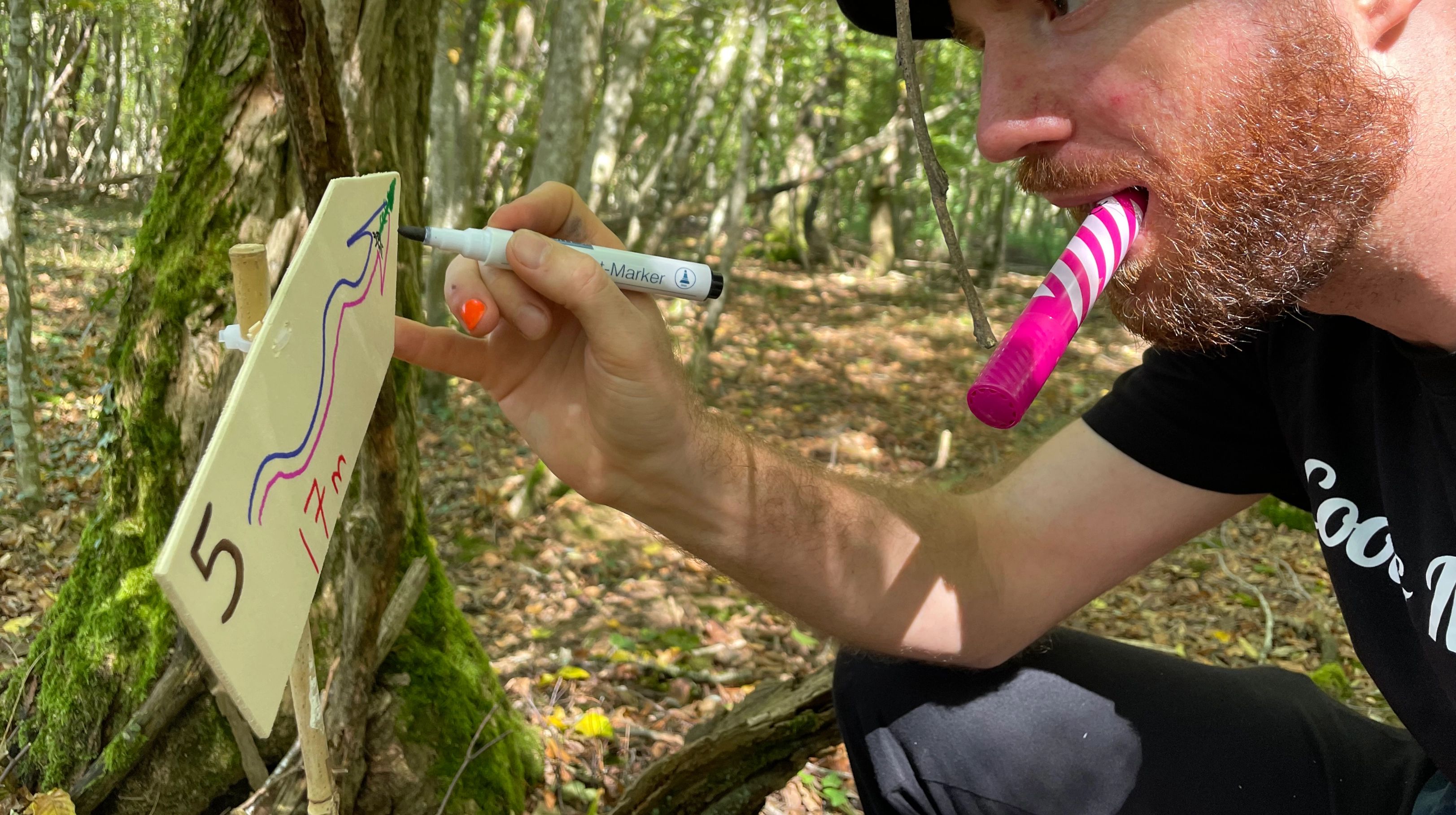 A man with a whistle in his mouth draws a route on a numbered wooden sign in the forest
