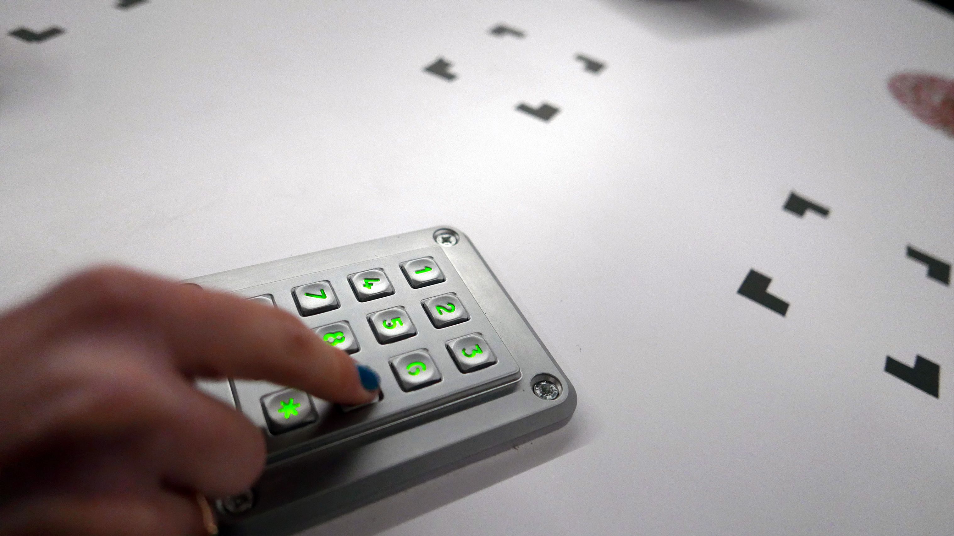 A finger presses a lit keypad on a white table covered in black puzzle pieces