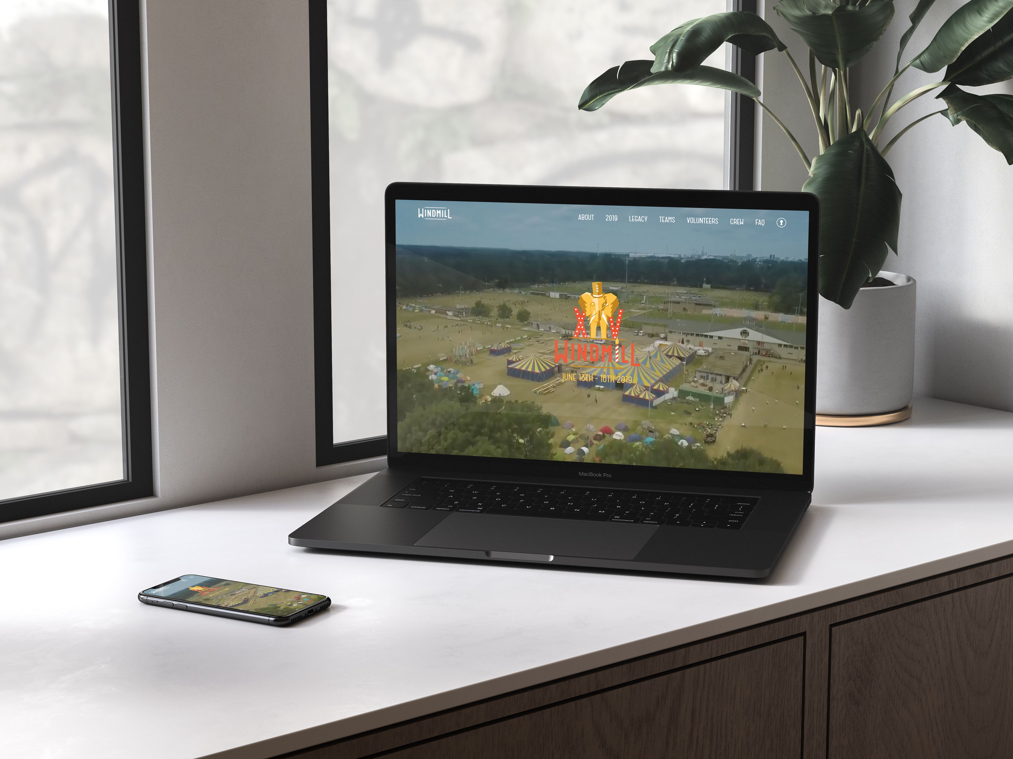 A laptop and phone on a windowsill showing the Windmill website with an aerial photo of the tournament
