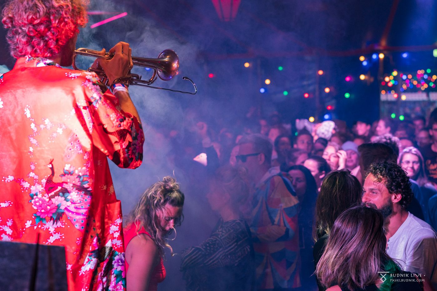 A trumpet player in a red kimono performs for a dancing crowd at a party in a tent