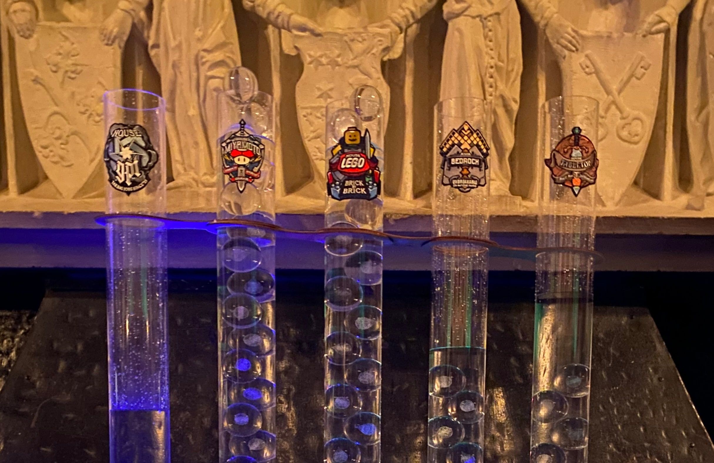 Five tall glass cylinders with house crests, partly filled with crystal orbs, in front of a carved stone wall