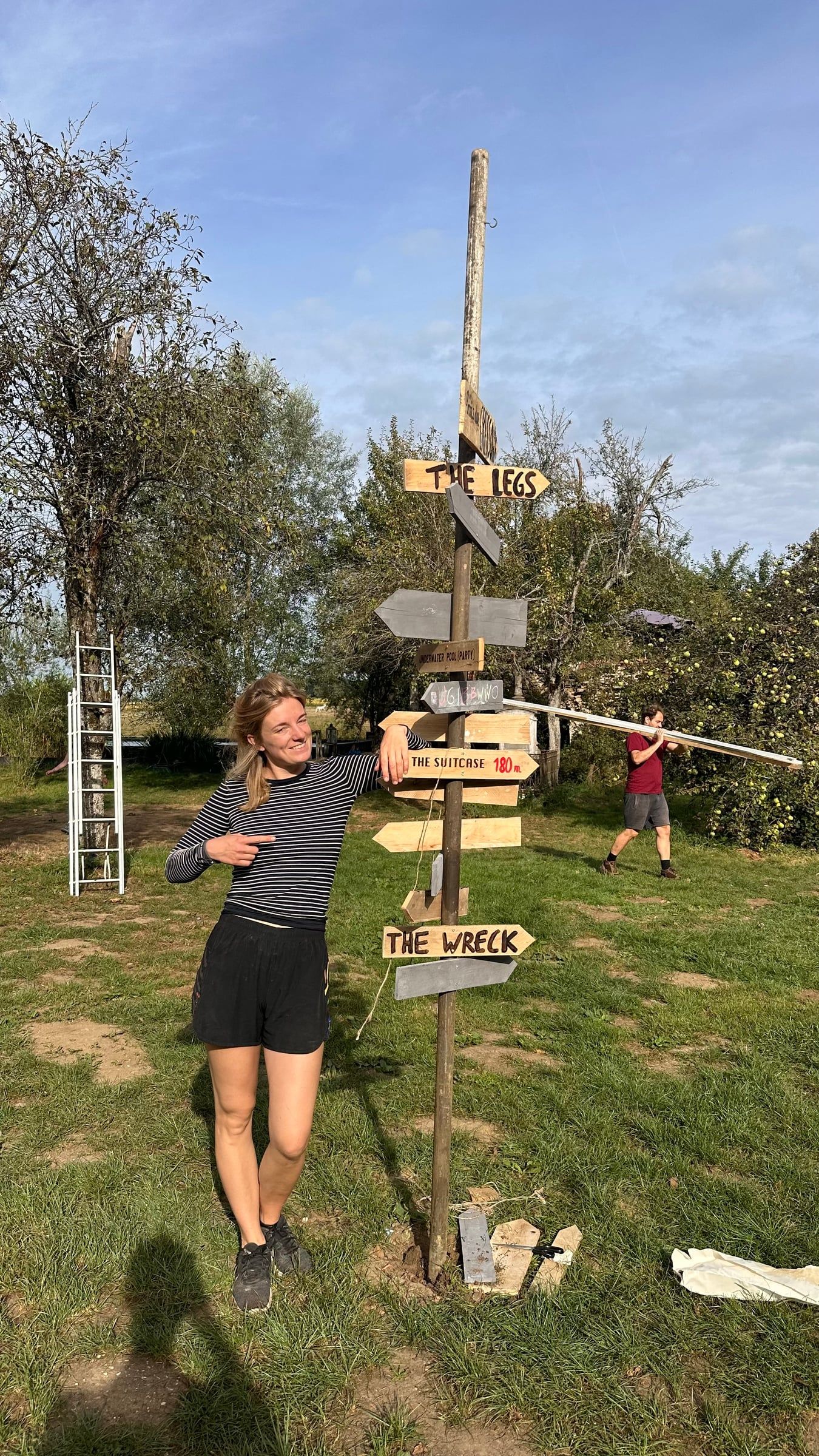 A woman leans against a festival signpost full of hand-painted arrows, one of them pointing to The Suitcase