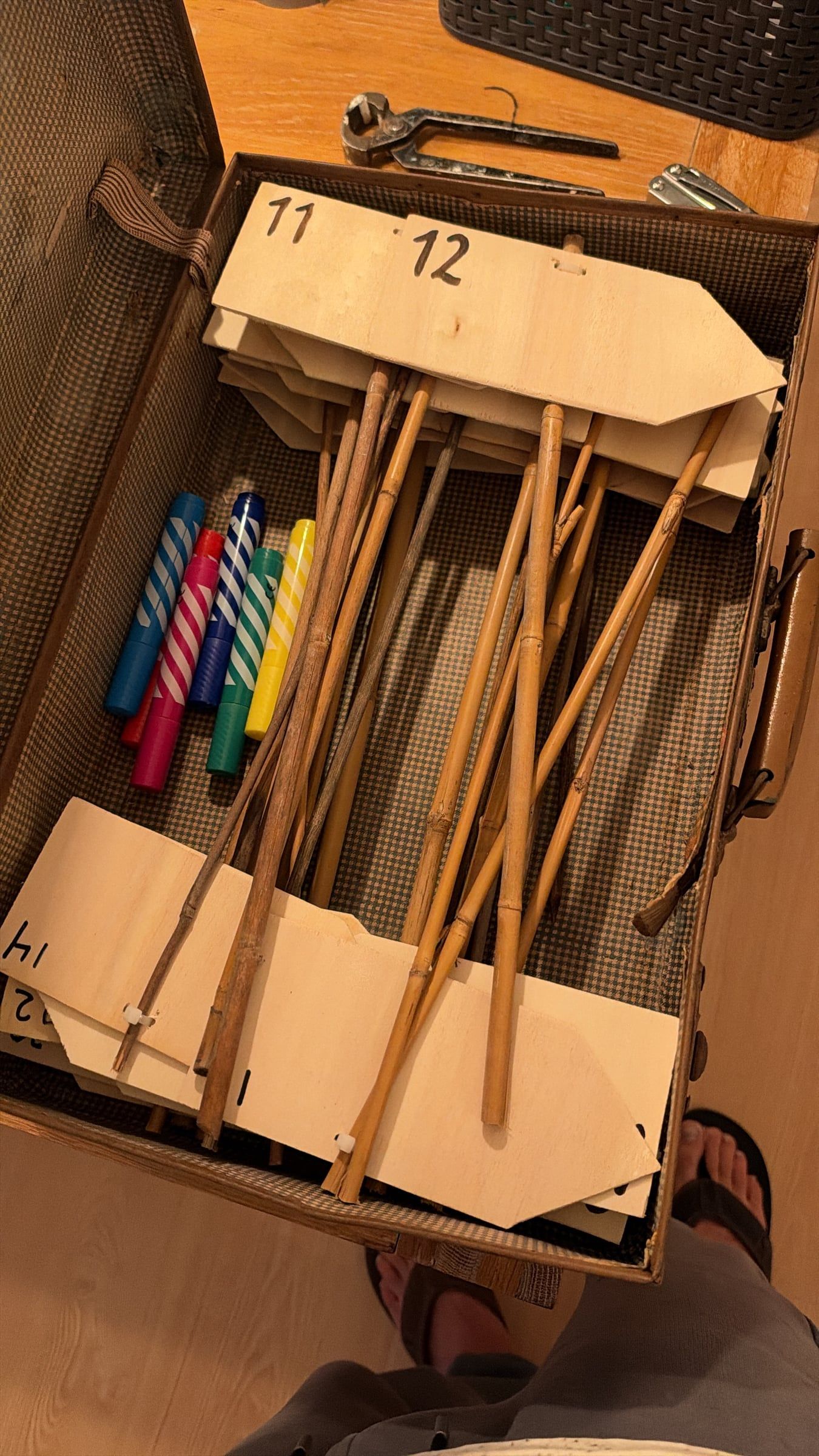An open vintage suitcase holding numbered wooden arrow signs on bamboo poles and a row of colourful markers